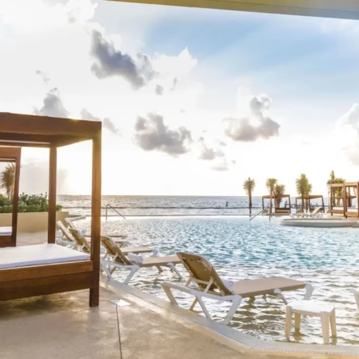 Covered daybed and oceanfront pool with lounge chairs under soft morning light at Sensira Resort.