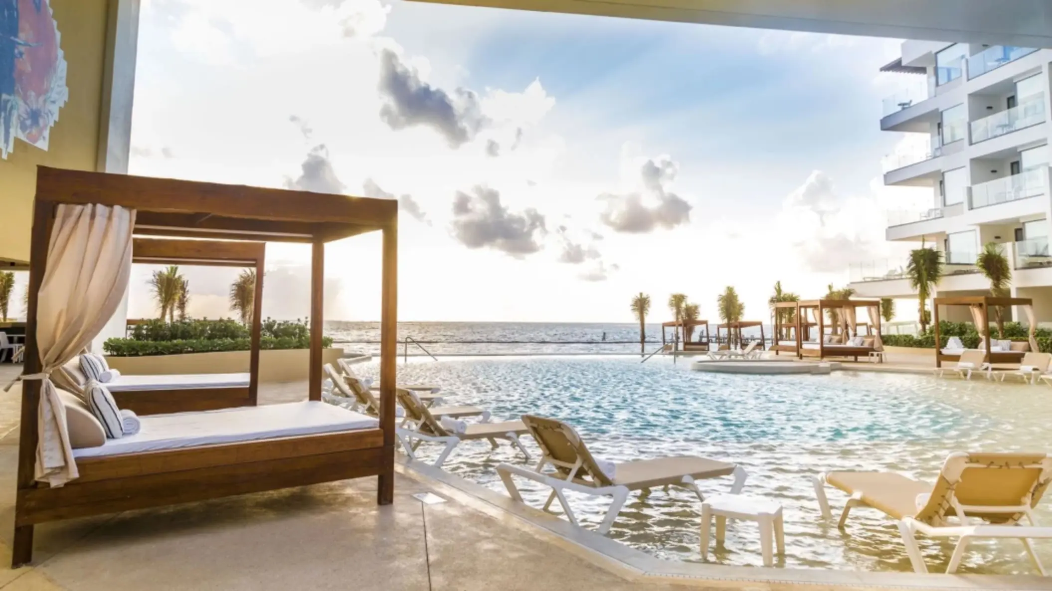 Covered daybed and oceanfront pool with lounge chairs under soft morning light at Sensira Resort.