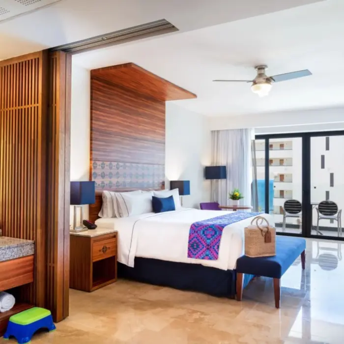 Modern oceanview room with king bed, colorful runner, balcony seating, and open vanity with granite countertop.