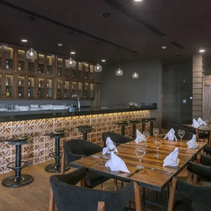 Rustic-style indoor bar with wood cabinets, hanging lights, tiled bar front, and intimate dining setup with dark chairs.