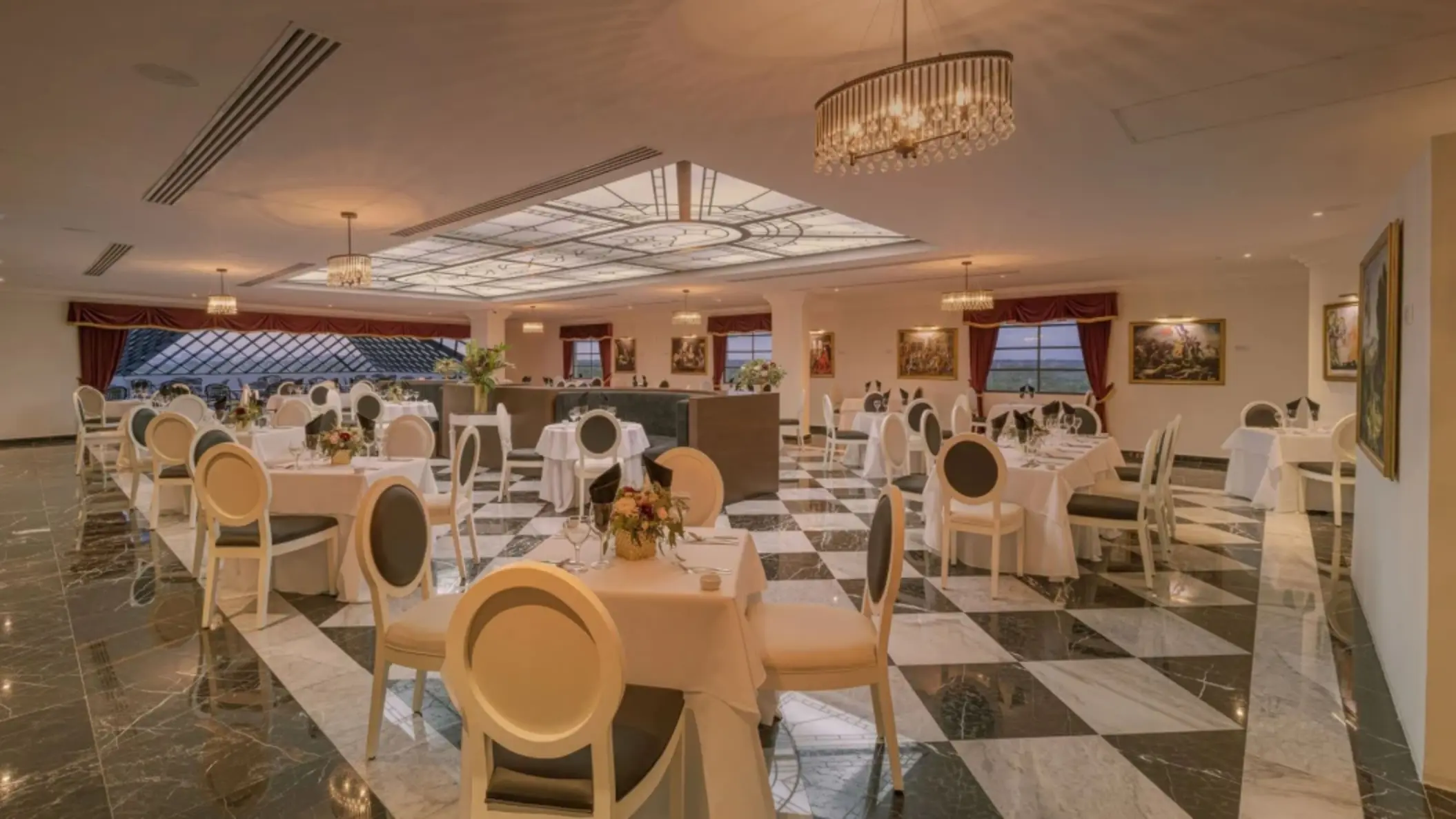Refined dining room with black and white floors, chandeliers, and round tables set for dinner service.