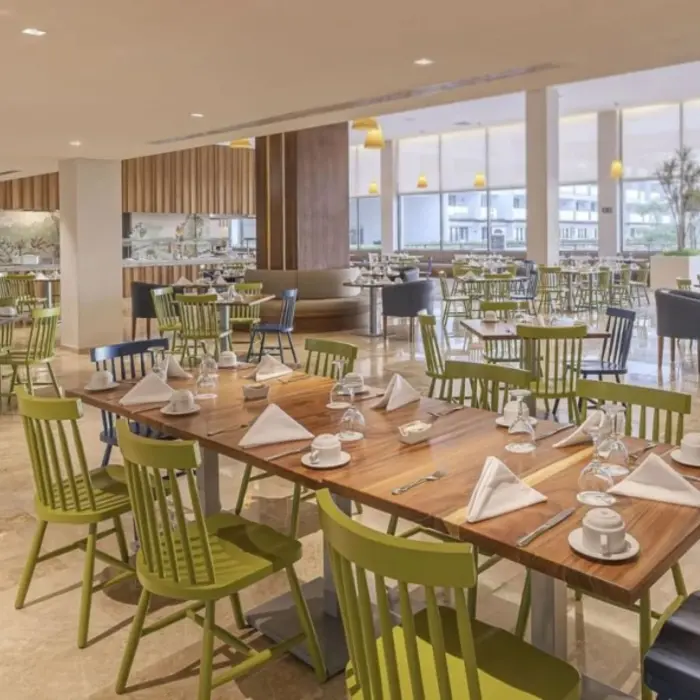 Casual buffet-style restaurant with green and blue chairs, natural light, and open seating layout.