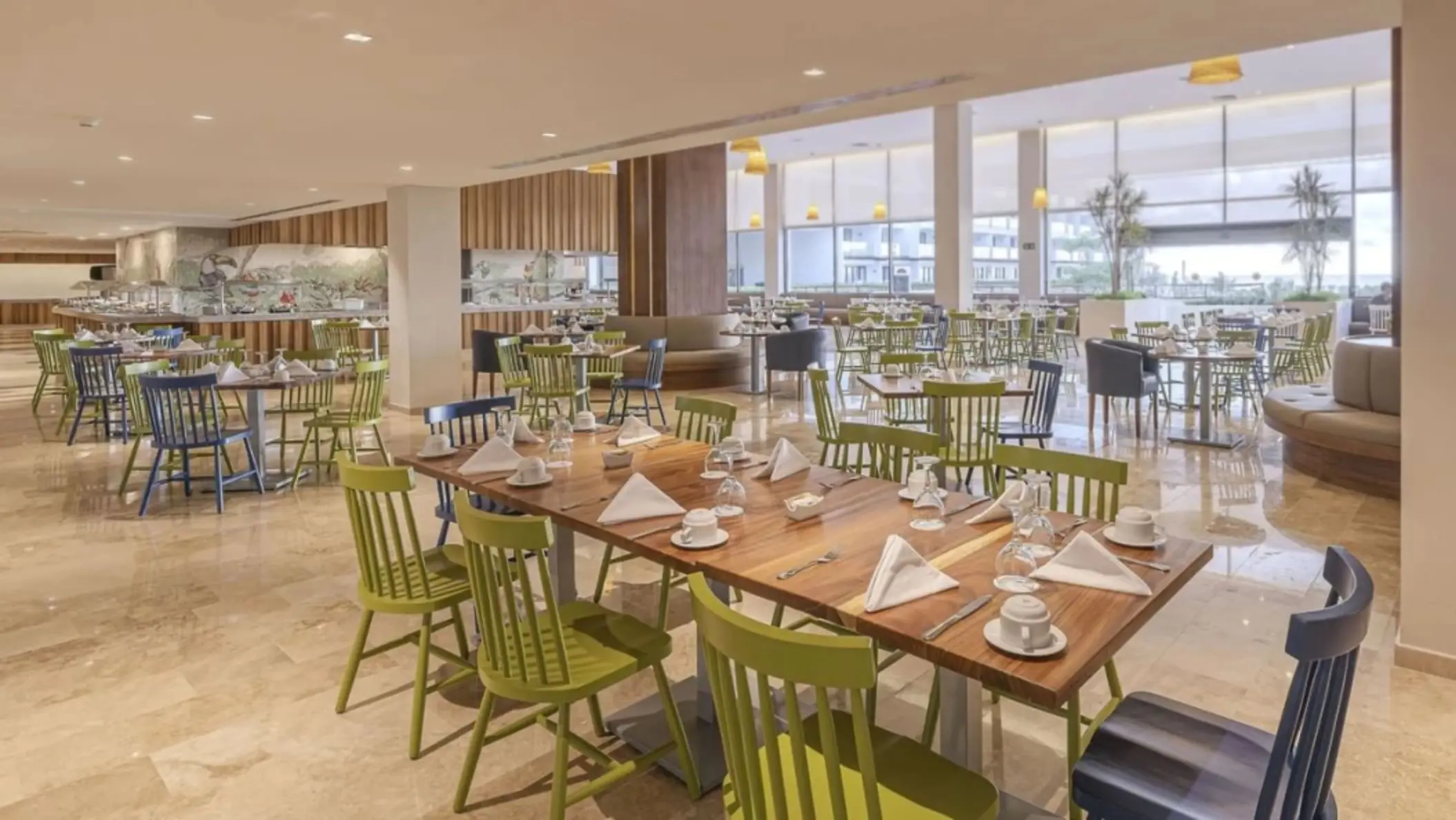 Casual buffet-style restaurant with green and blue chairs, natural light, and open seating layout.