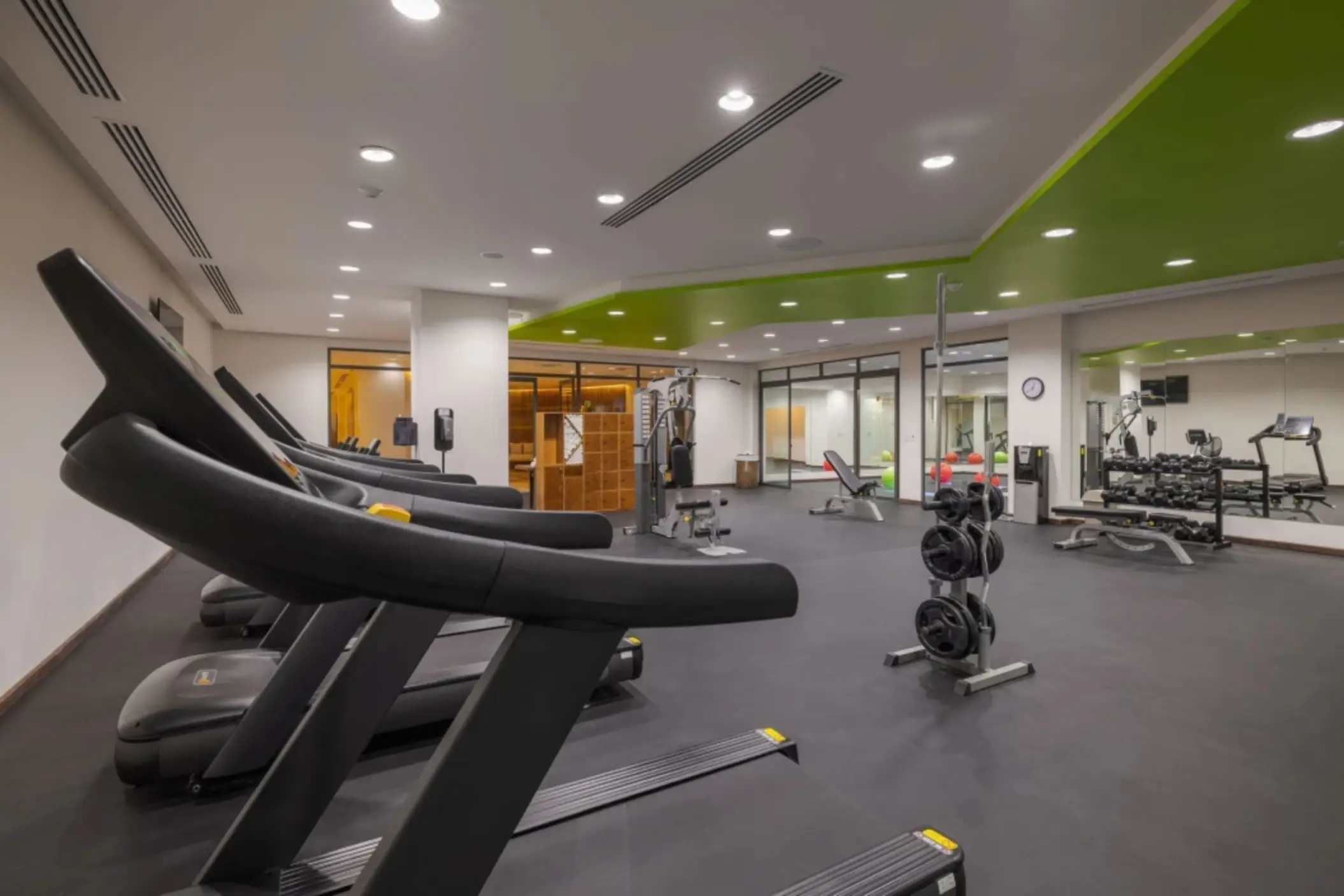 Modern gym with treadmills, weight training equipment, and green ceiling accent at Sensira Resort.