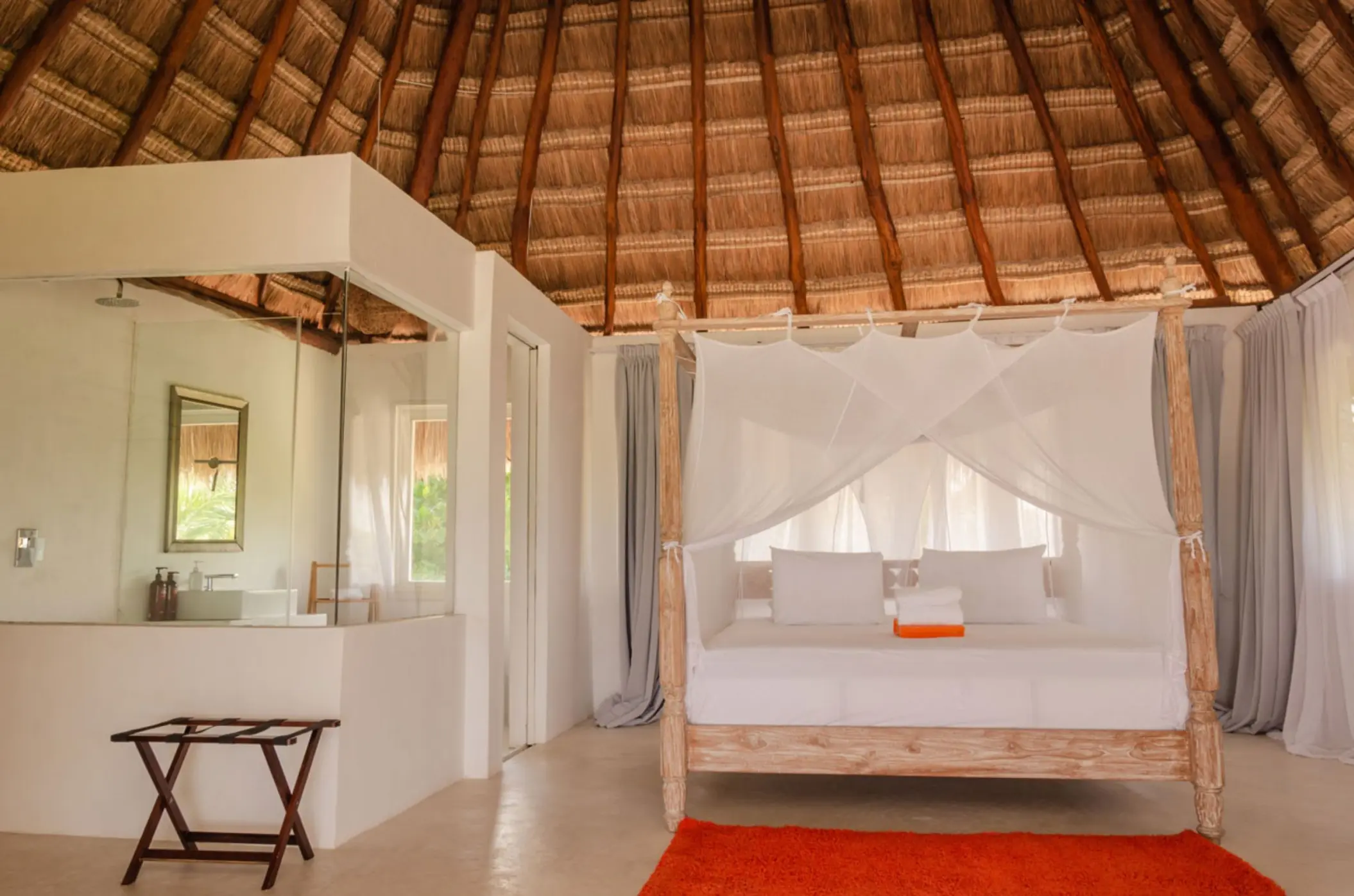 Interior of a casita with a king-sized bed draped in white netting, a thatched roof, and orange rug.