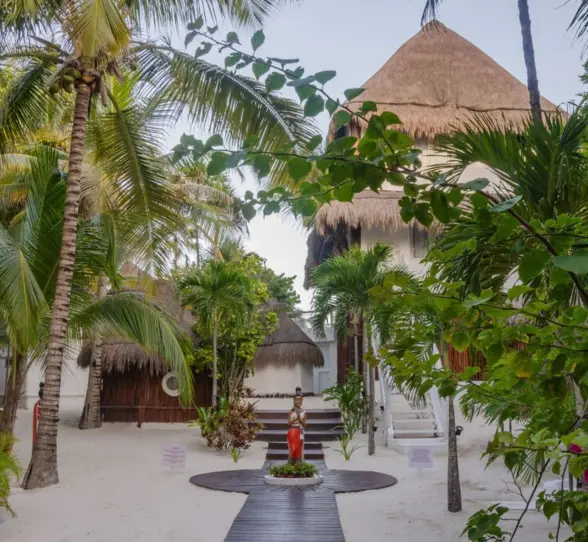 The entrance path through lush greenery and palm trees, leading toward thatched-roof buildings.