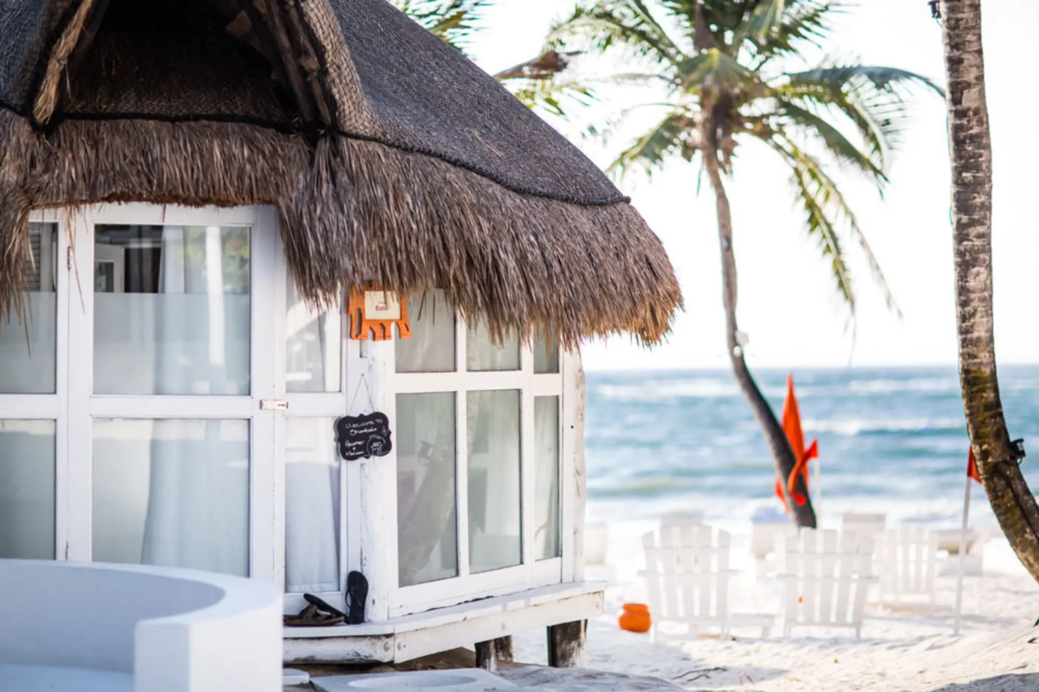 Close-up exterior of a beach casita with a thatched roof, white walls, and view of the beach and ocean.