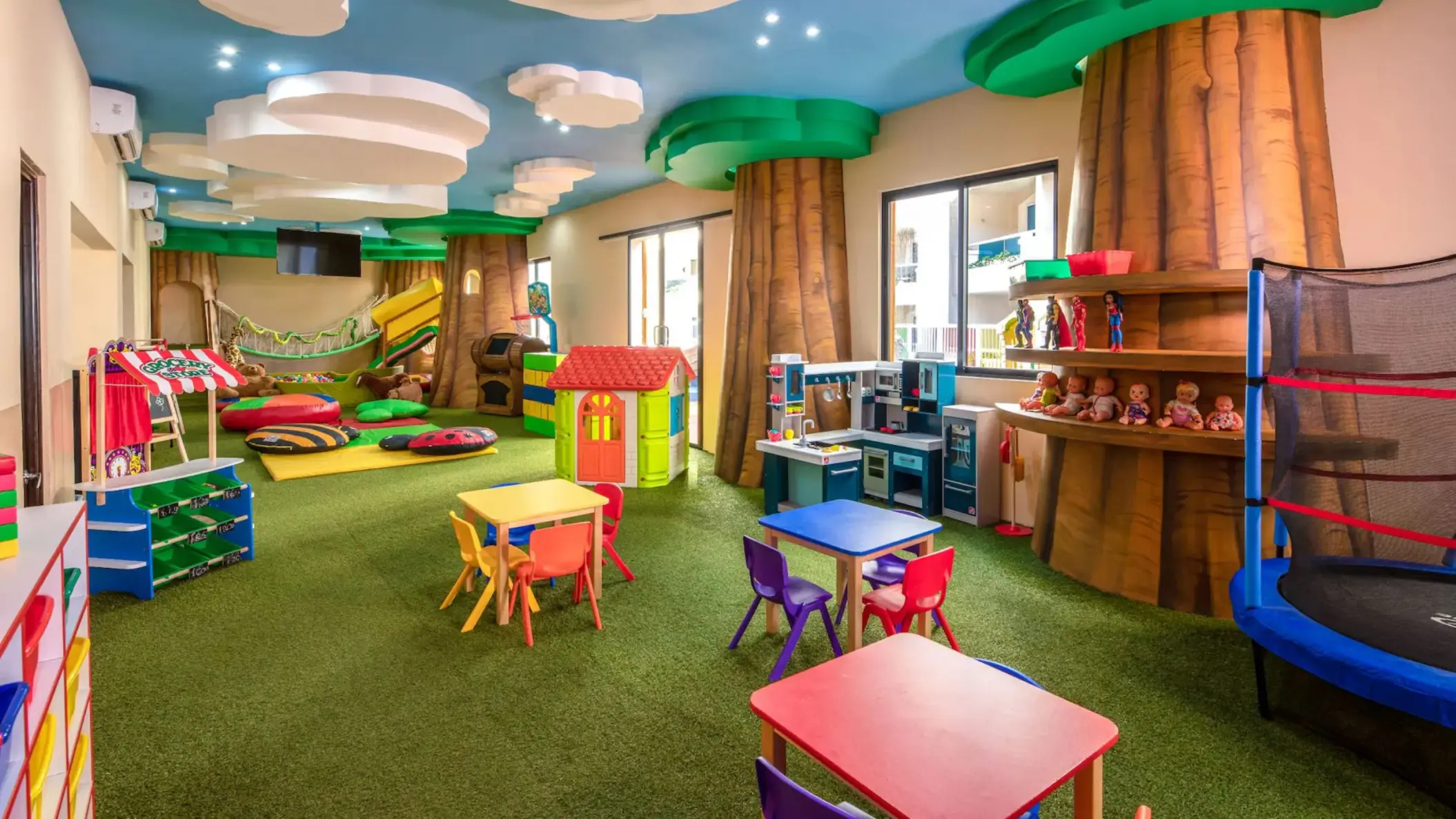 A bright and colorful kids club with a playhouse, slide, arts and crafts tables, and a trampoline.