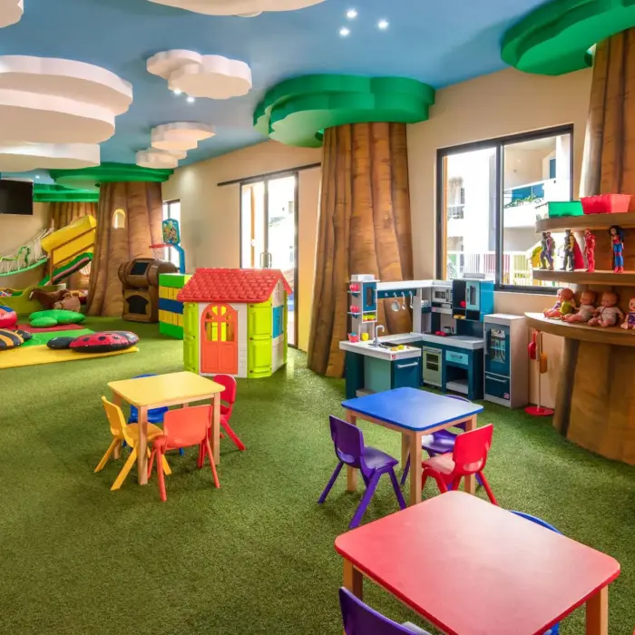 A bright and colorful kids club with a playhouse, slide, arts and crafts tables, and a trampoline.