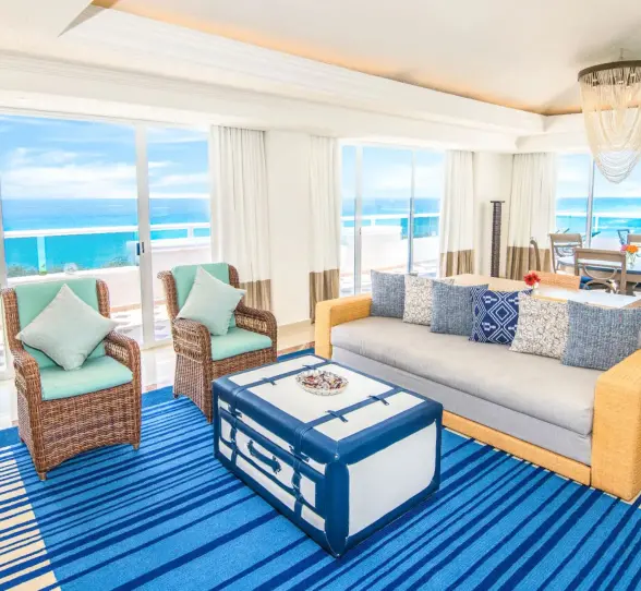 The living area of a presidential suite with a couch, chairs, and a breathtaking ocean view.