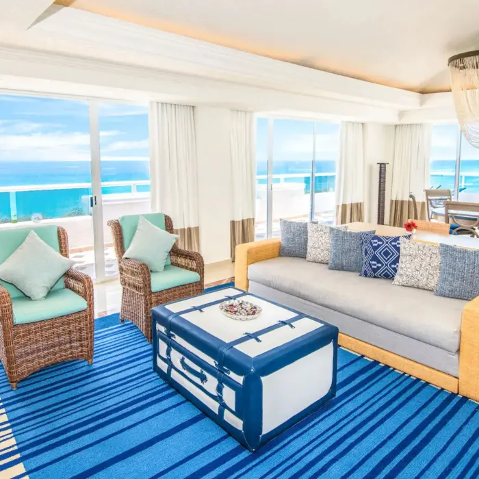 The living area of a presidential suite with a couch, chairs, and a breathtaking ocean view.