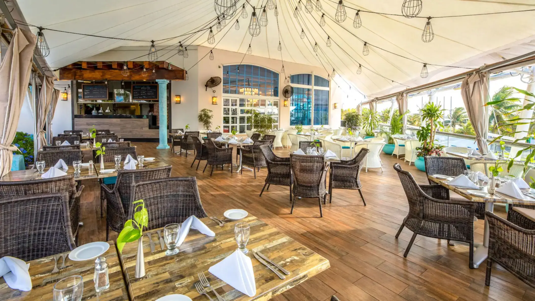 An upscale indoor restaurant with wicker chairs, string lights, and a full bar.