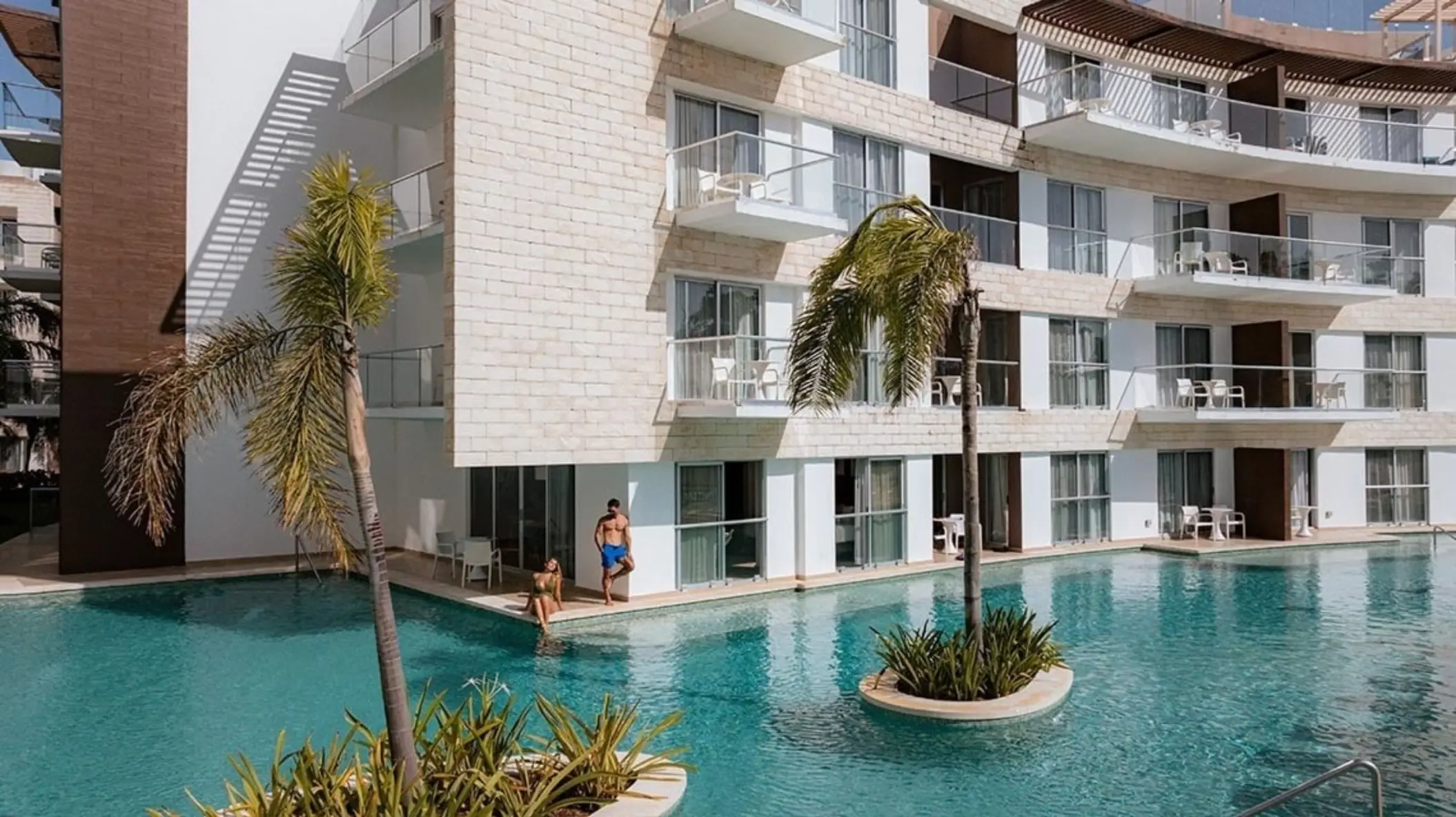 Exterior of swim-up suites at The Fives Beach Hotel, with guests enjoying direct access to a refreshing pool surrounded by palm trees and modern architecture.
