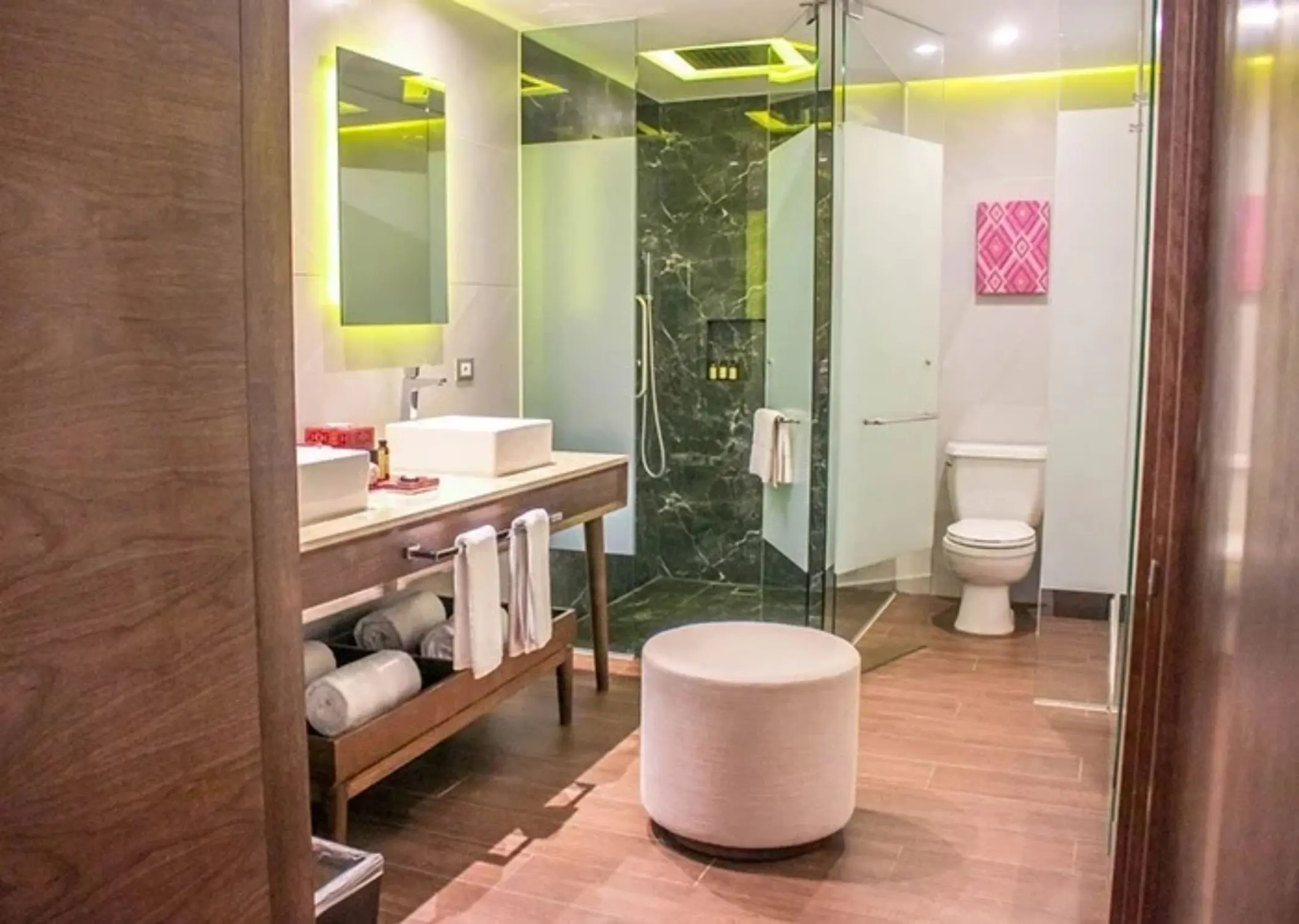 Modern bathroom with green accent lighting, marble shower, and double vanity.