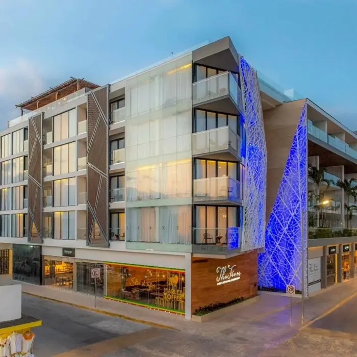 Exterior view of The Fives Downtown Hotel lit up in blue with visible balconies and Marley Coffee at street level.
