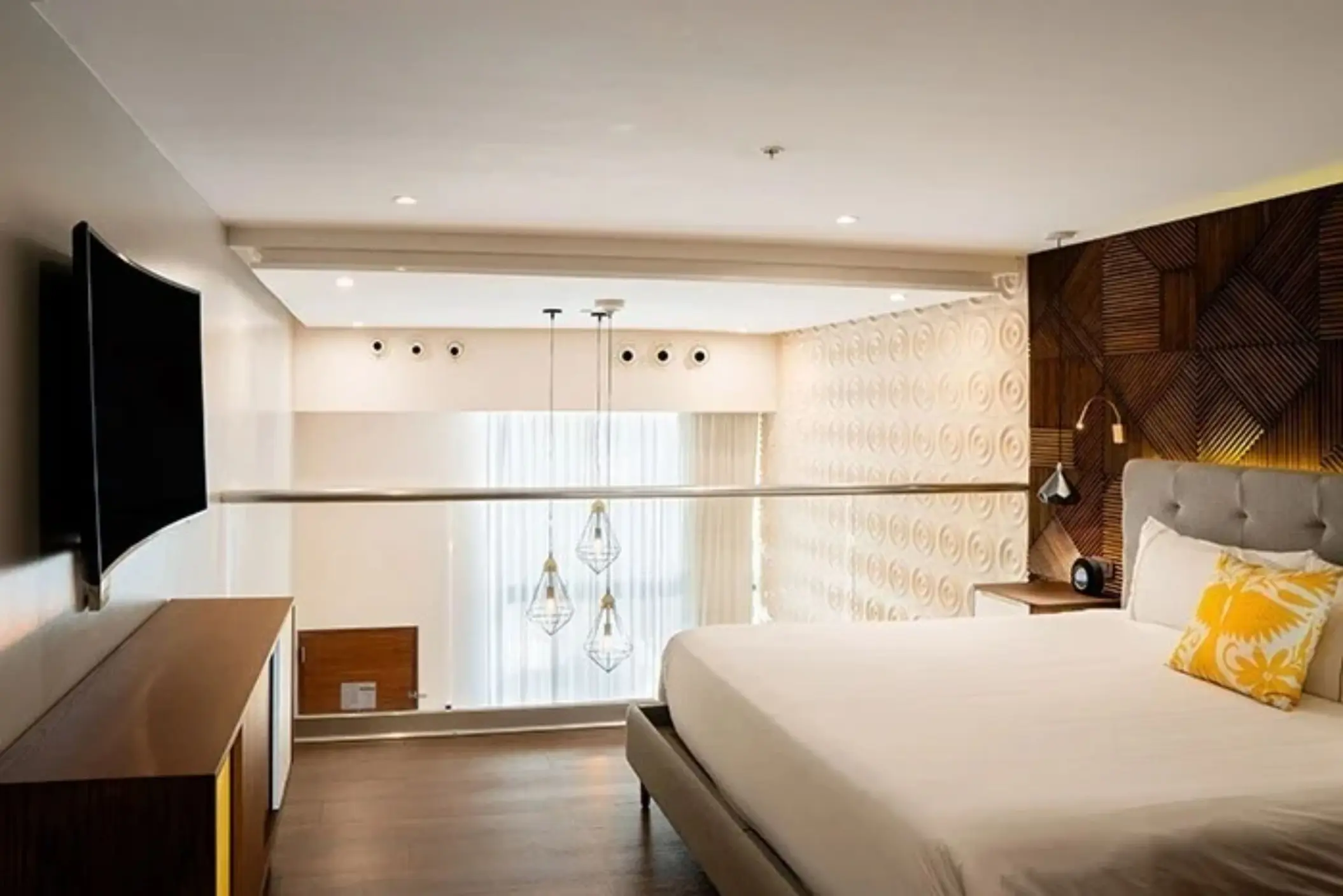 Loft-style room with king bed, wood finishes, hanging lights, and overlook view of floor-to-ceiling windows.
