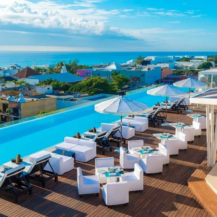 Stylish rooftop infinity pool with ocean views, white lounge furniture, and umbrellas overlooking downtown Playa.