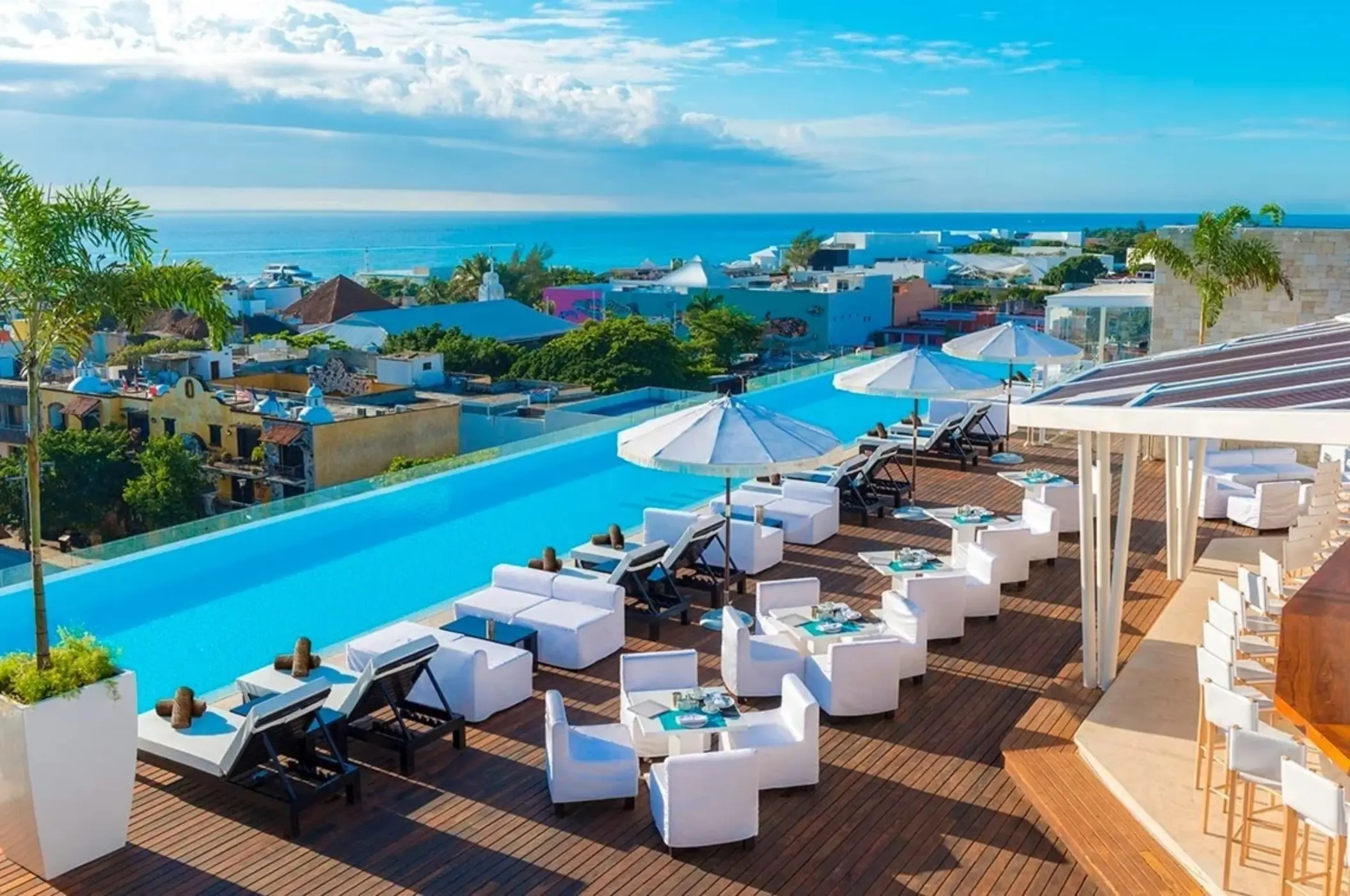 Stylish rooftop infinity pool with ocean views, white lounge furniture, and umbrellas overlooking downtown Playa.