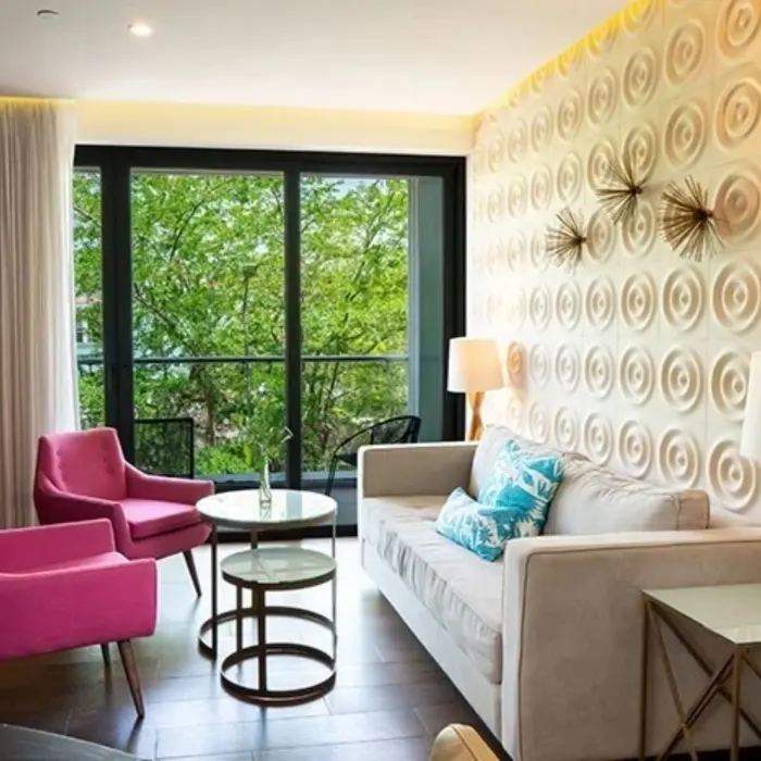 Bright living area with cream sofa, pink chairs, glass tables, and balcony views surrounded by lush greenery.
