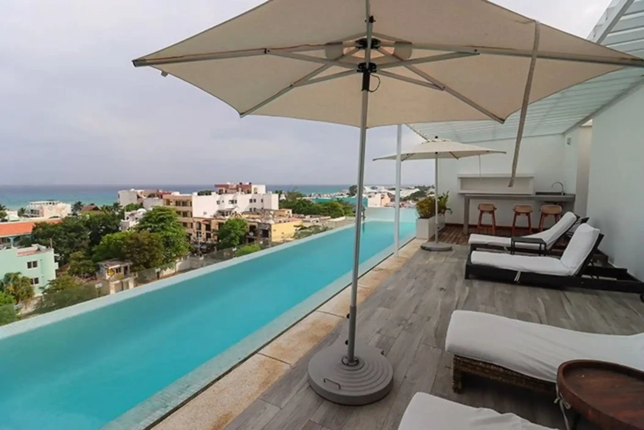 Rooftop pool deck with loungers, umbrellas, and ocean views overlooking Playa del Carmen from The Fives Downtown.