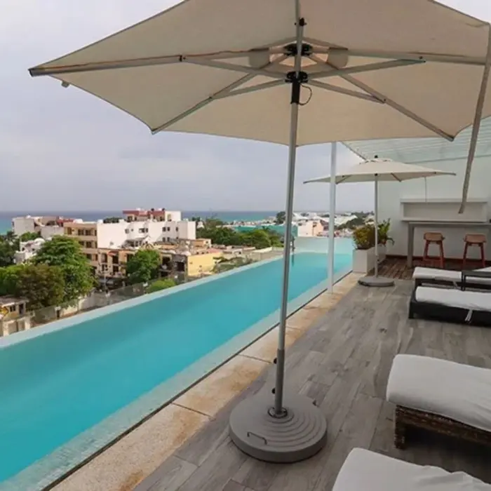 Rooftop pool deck with loungers, umbrellas, and ocean views overlooking Playa del Carmen from The Fives Downtown.