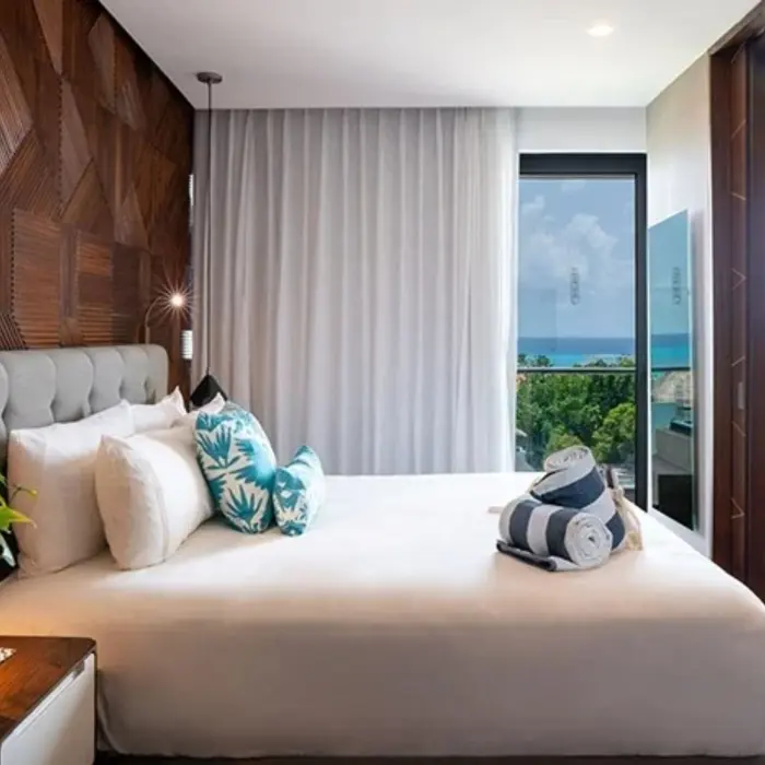 Oceanview suite with king bed, wood paneling, white curtains, and balcony overlooking lush greenery and sea.