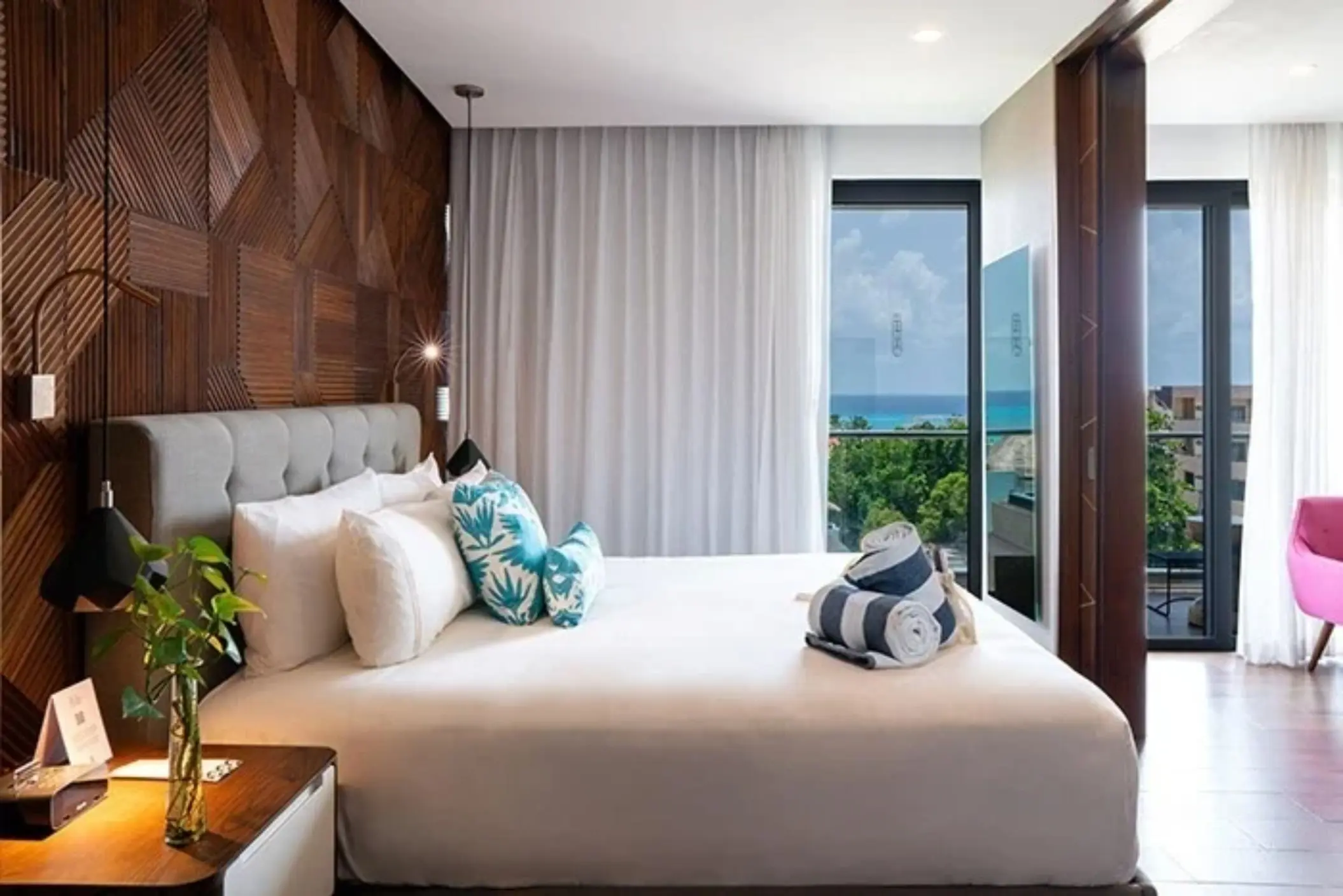 Oceanview suite with king bed, wood paneling, white curtains, and balcony overlooking lush greenery and sea.