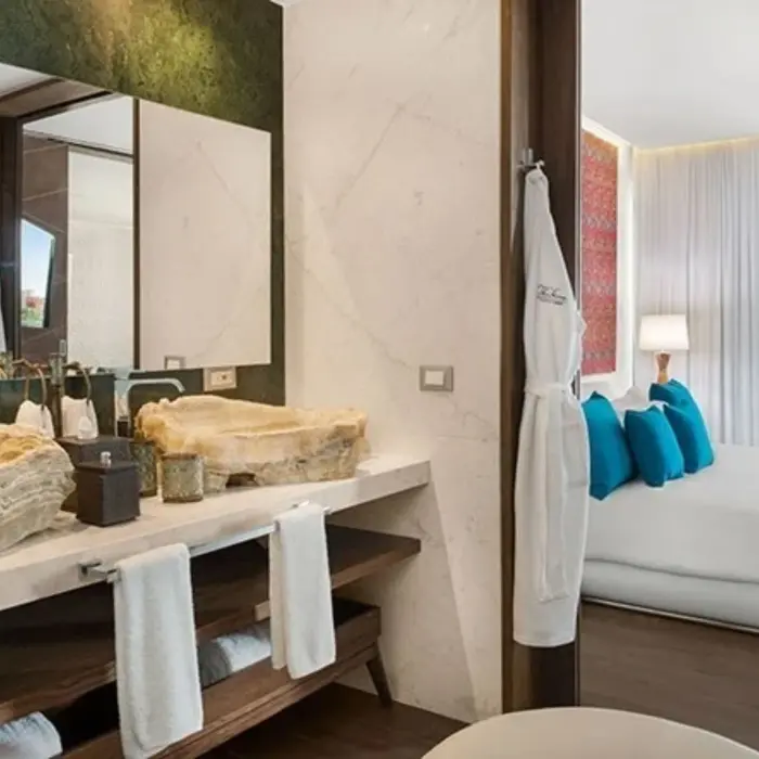 Elegant bathroom with onyx-style stone sinks, wall-length mirror, and view of a bedroom with blue accents.