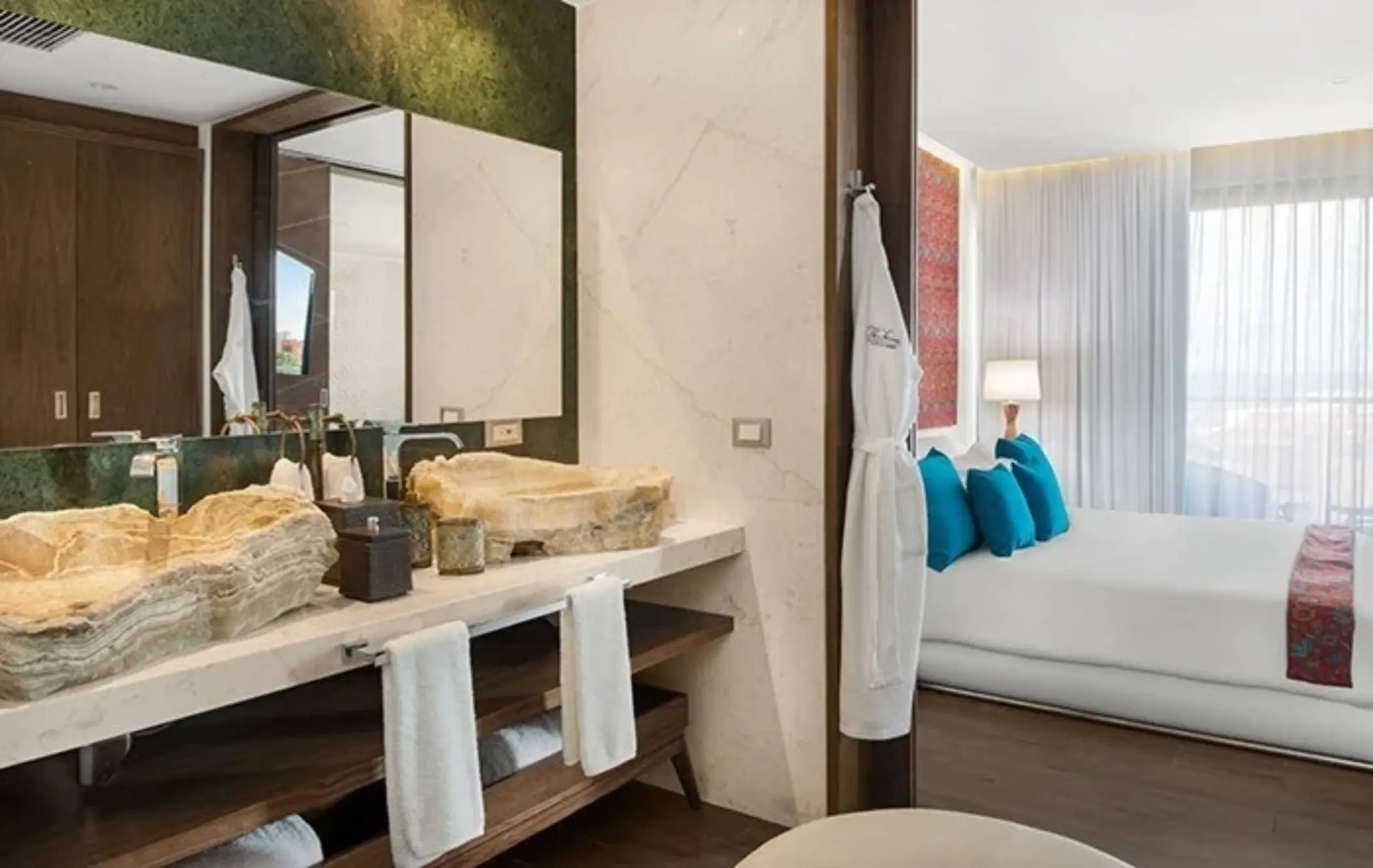 Elegant bathroom with onyx-style stone sinks, wall-length mirror, and view of a bedroom with blue accents.