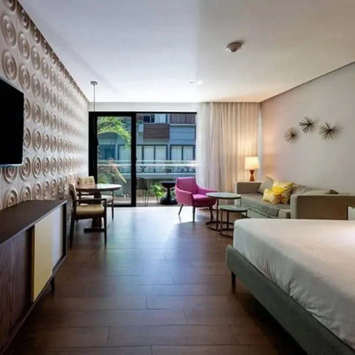 Open-plan suite with wood floors, a king bed, and modern furnishings, plus balcony view of courtyard greenery.