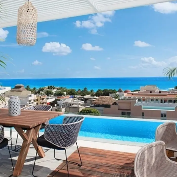 Rooftop terrace with plunge pool, ocean view, wooden table, and stylish woven chairs under hanging lanterns.