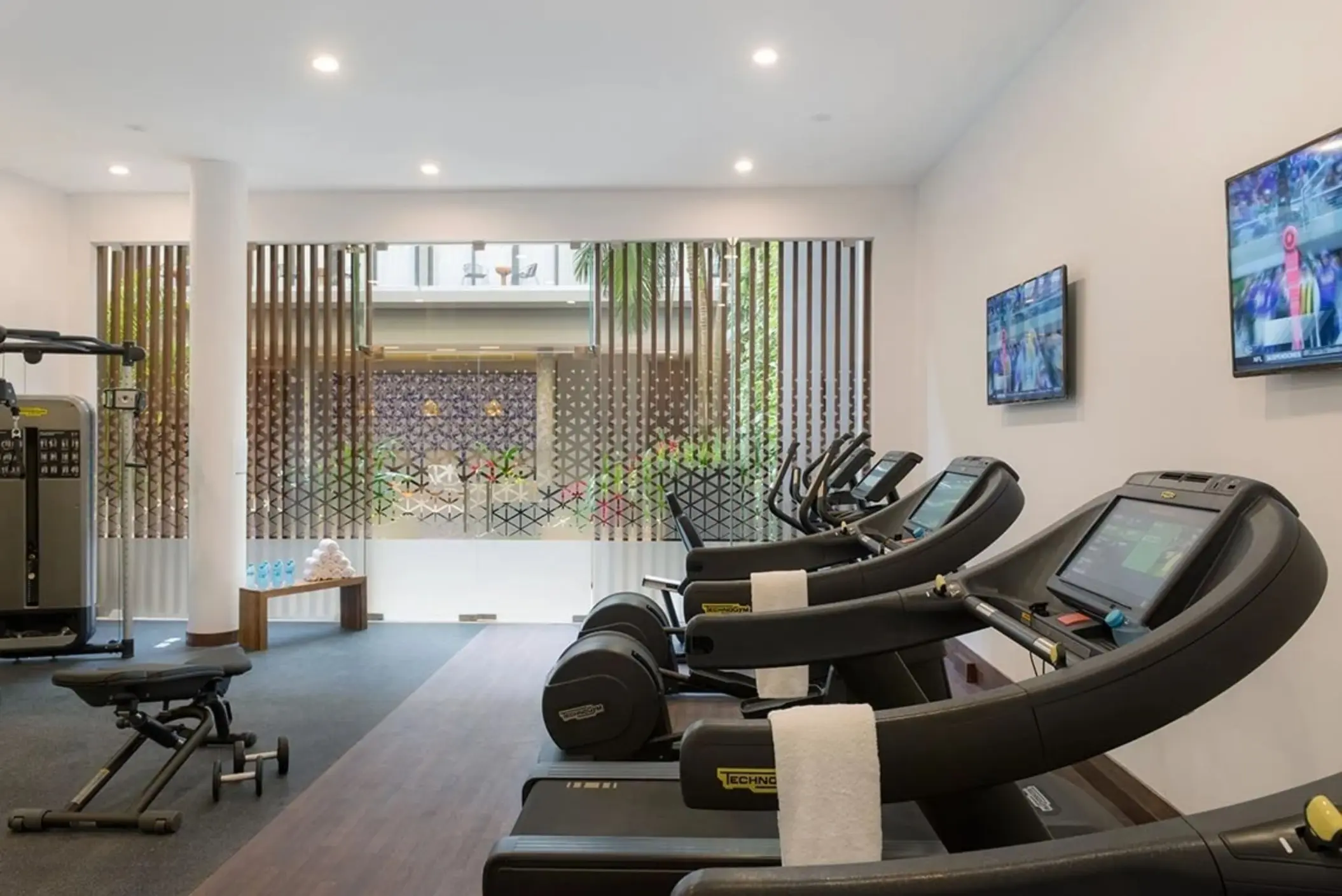 Resort fitness center with Technogym equipment, flat-screen TVs, and natural light.