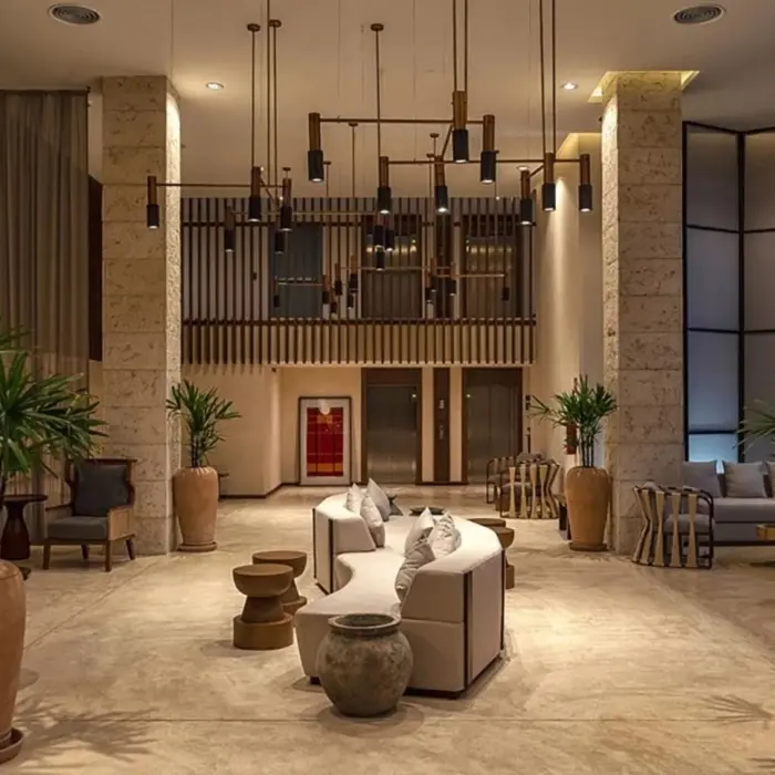 Spacious hotel lobby with modern lighting, natural stone pillars, large potted plants, and cozy seating areas.