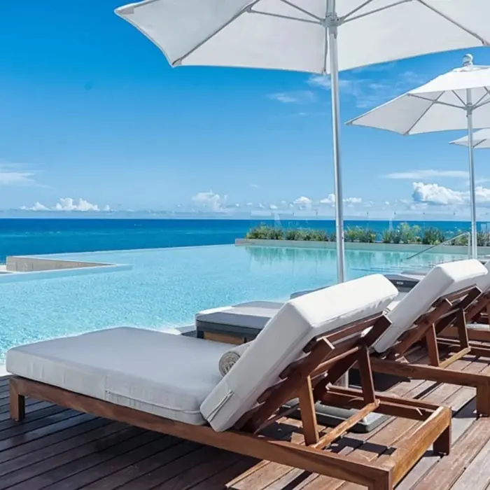 Infinity pool with white umbrellas and wooden loungers facing the bright blue Caribbean Sea under a clear sky.