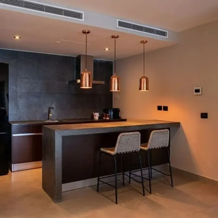 Stylish kitchenette with dark stone countertops, copper pendant lights, and two woven barstools.