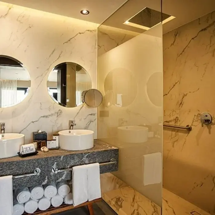 Marble bathroom with dual sinks, round mirrors, walk-in rain shower, and elegant lighting.