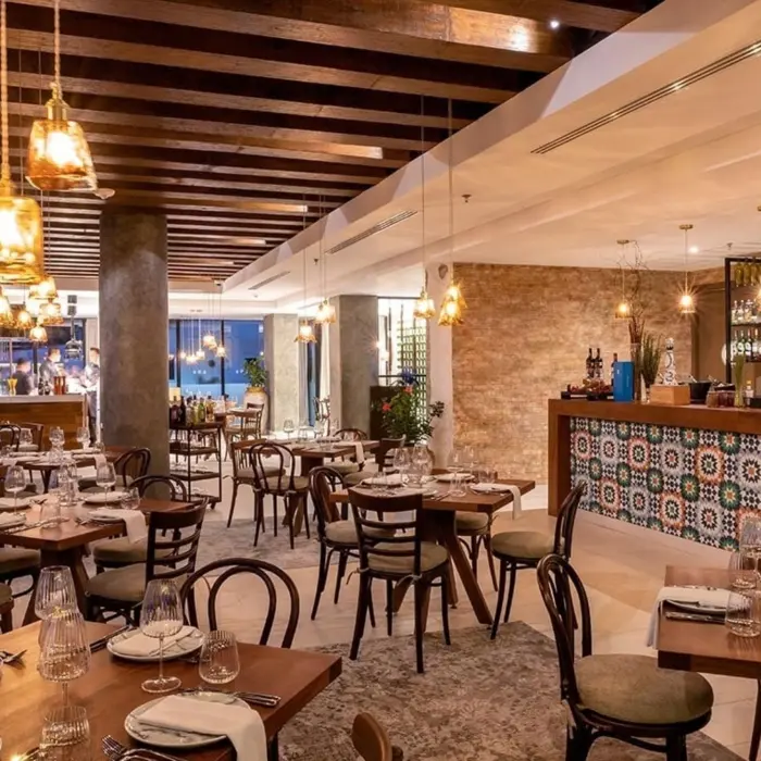 Elegant restaurant with warm lighting, wood beam ceiling, and colorful tiled bar surrounded by rustic decor.