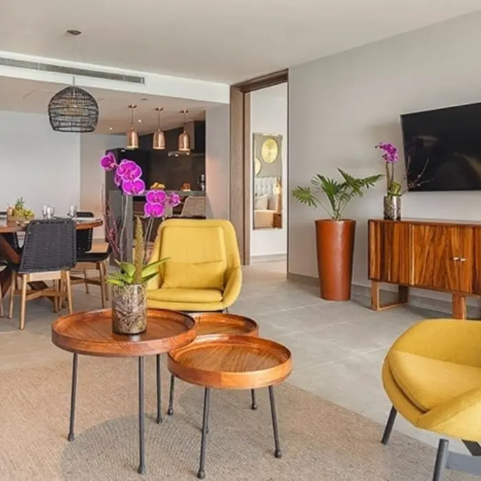 Bright suite with yellow chairs, wood coffee tables, and dining area featuring orchids and modern decor.