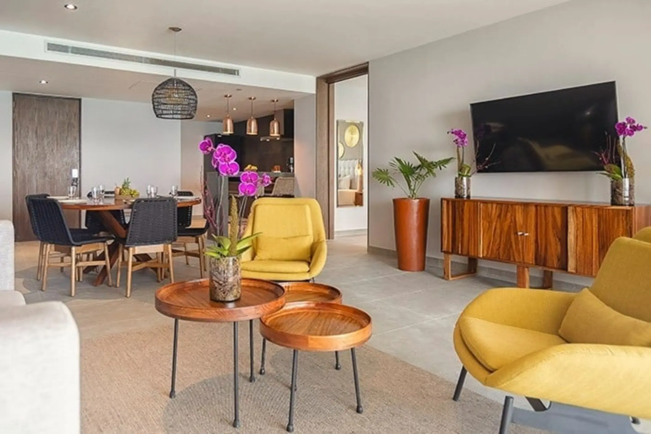 Bright suite with yellow chairs, wood coffee tables, and dining area featuring orchids and modern decor.