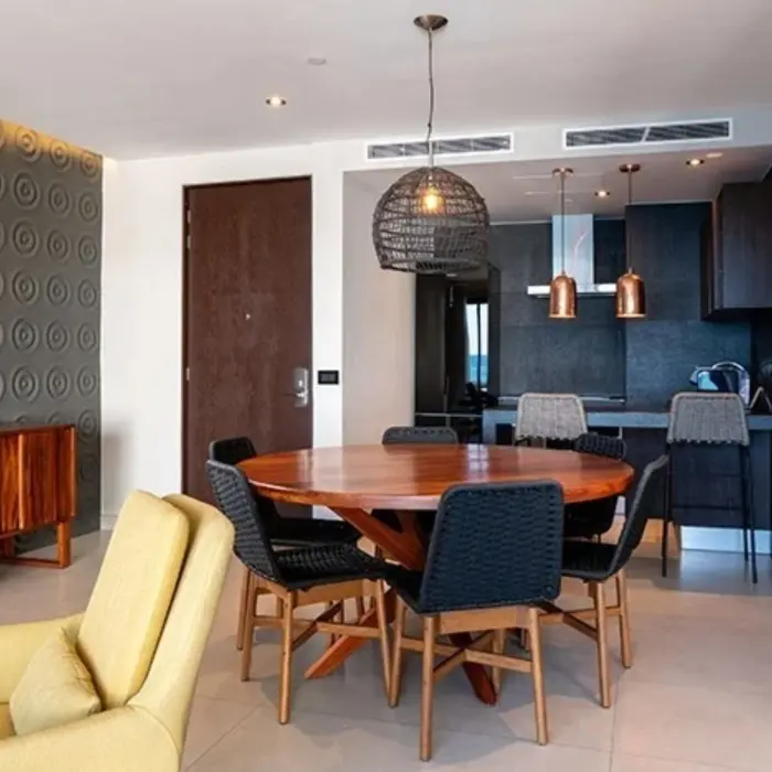 Cozy dining area with round table, woven pendant light, and kitchenette featuring copper accents and barstools.
