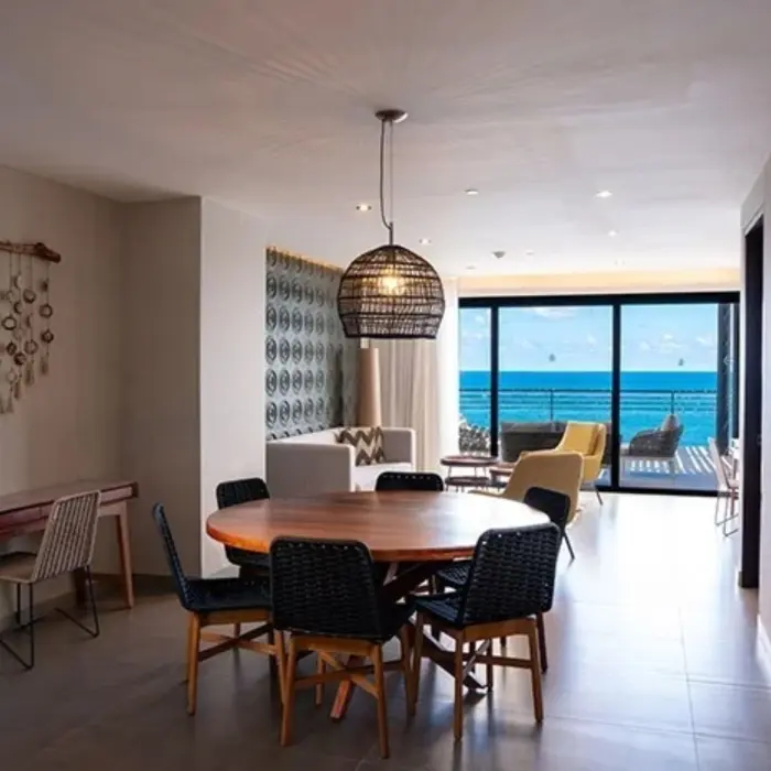 Dining area with woven pendant light and ocean view balcony in the distance through glass doors.