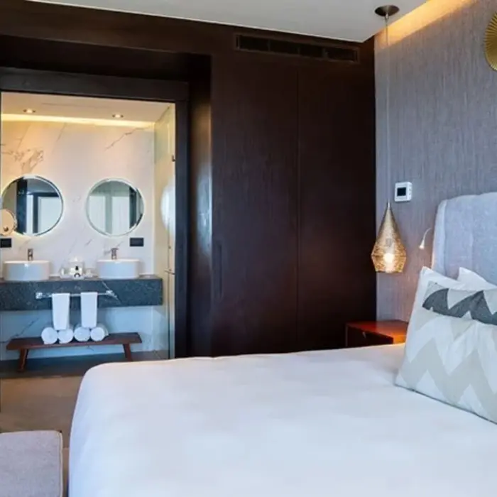Modern bedroom with king bed, dark wood accents, and open view into a double vanity bathroom.