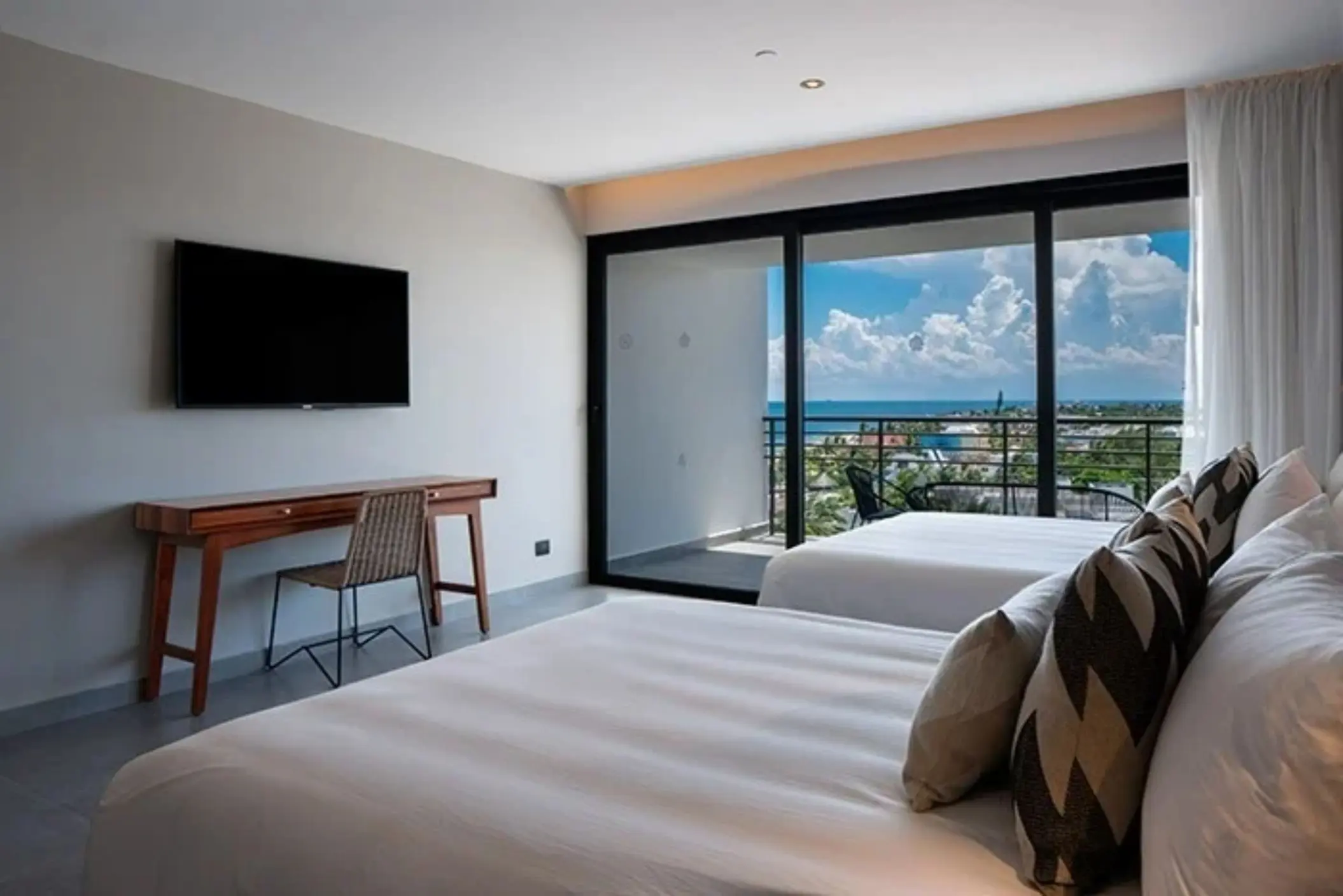 Spacious double room with oceanview balcony, writing desk, and flat screen TV above a sleek wood console.