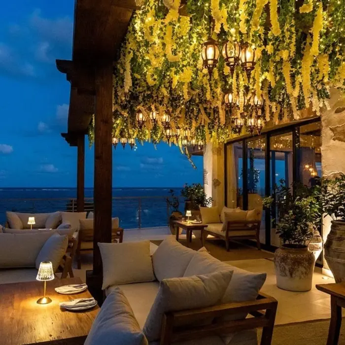 Romantic oceanview terrace with cozy seating, lantern lighting, and hanging greenery glowing under the evening sky.