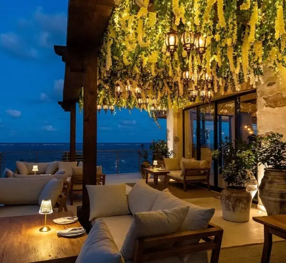 Romantic oceanview terrace with cozy seating, lantern lighting, and hanging greenery glowing under the evening sky.