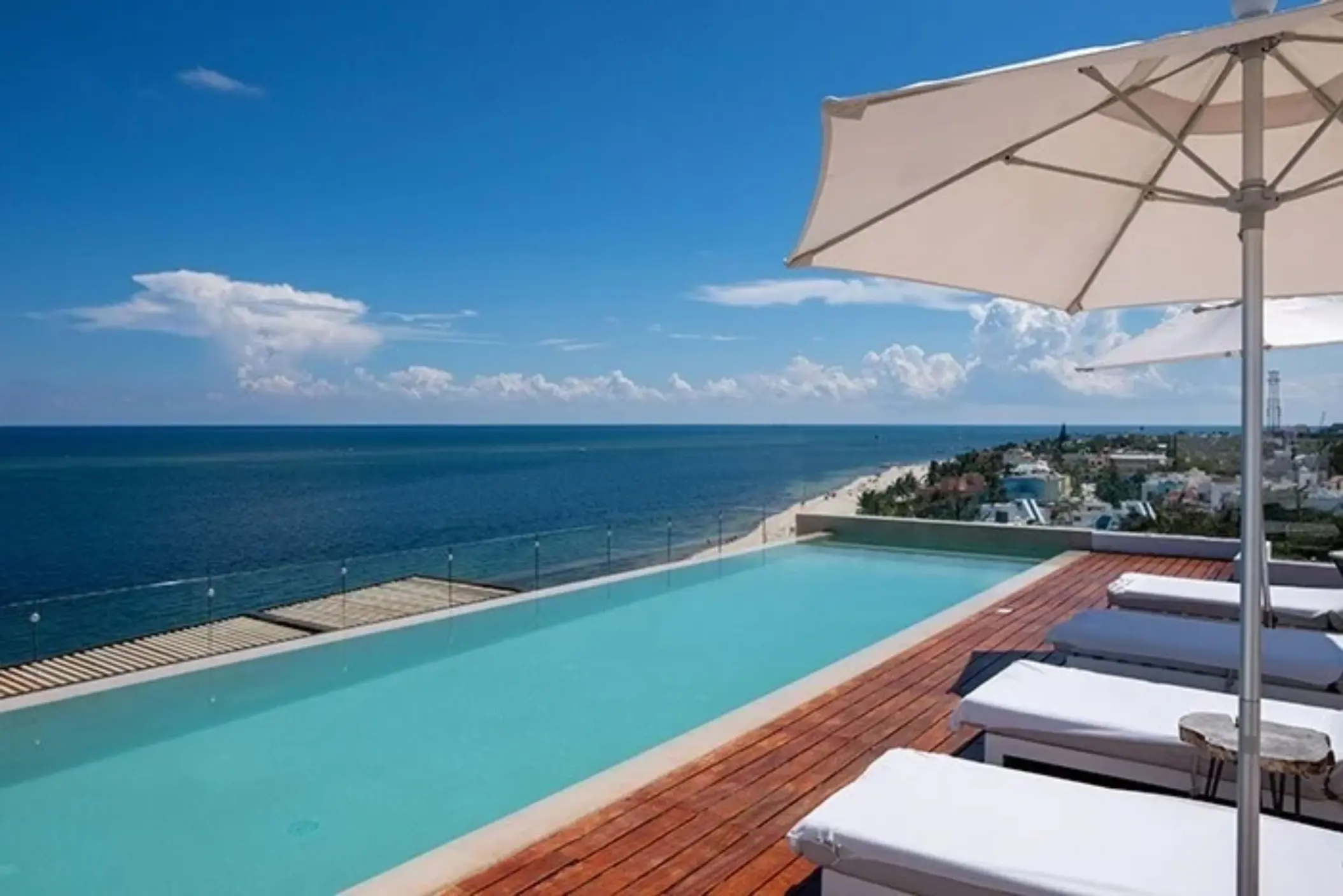 Rooftop infinity pool with loungers and parasols, offering expansive ocean views and a serene tropical vibe.