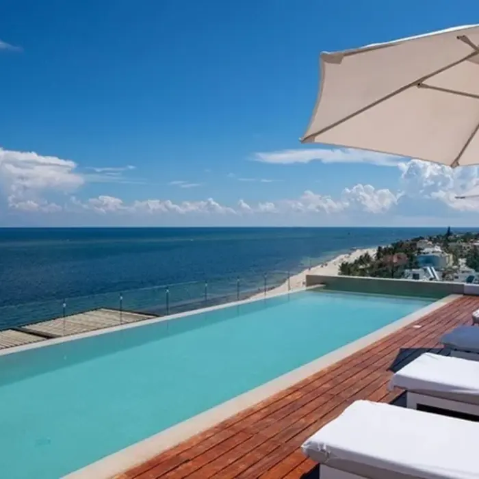 Rooftop infinity pool with loungers and parasols, offering expansive ocean views and a serene tropical vibe.