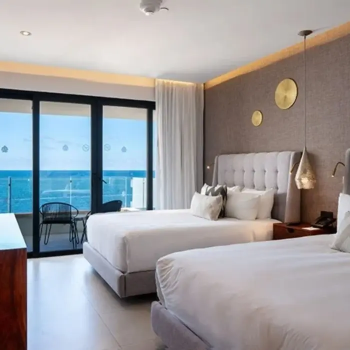 Contemporary room with two queen beds and private balcony overlooking the ocean through floor-to-ceiling glass doors.