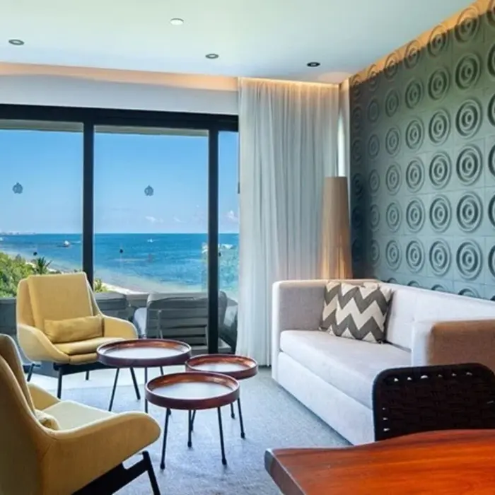 Bright suite lounge with ocean views, modern décor, and stylish furnishings through floor-to-ceiling windows.