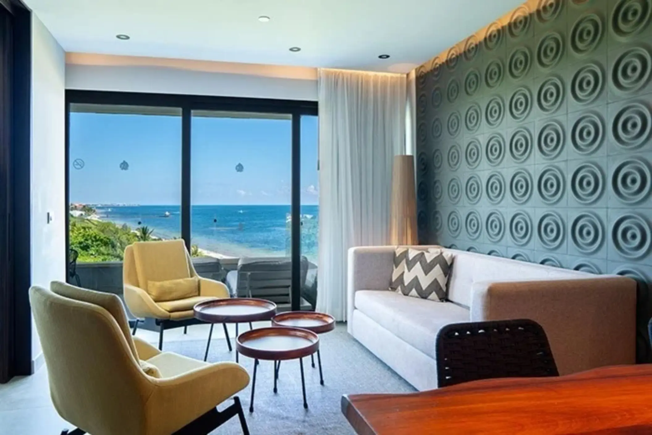 Bright suite lounge with ocean views, modern décor, and stylish furnishings through floor-to-ceiling windows.